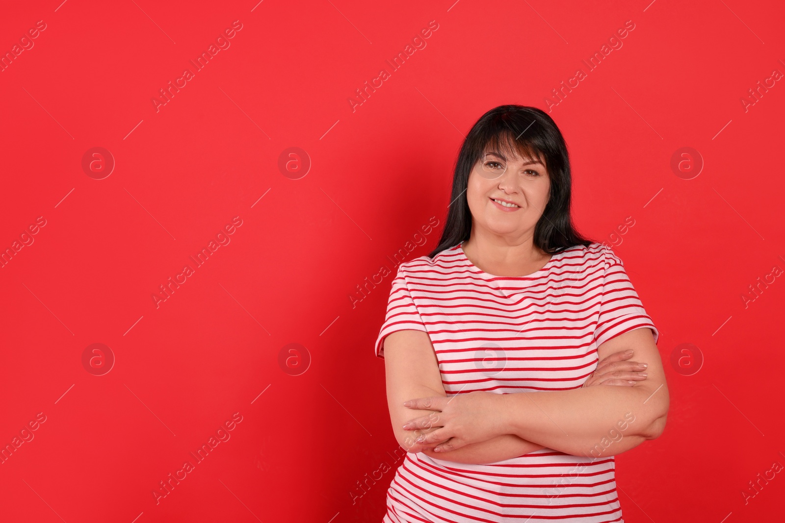 Photo of Beautiful overweight mature woman with charming smile on red background. Space for text