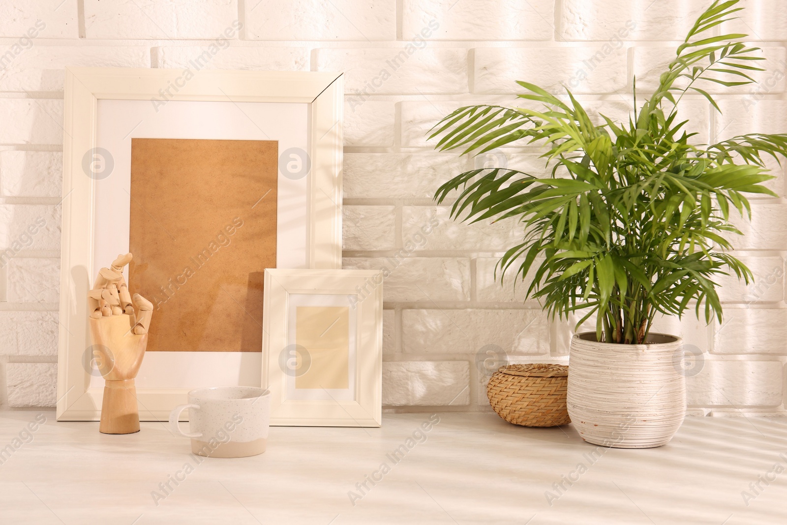 Photo of Stylish office workplace. Decor elements, plant and cup on white table near brick wall