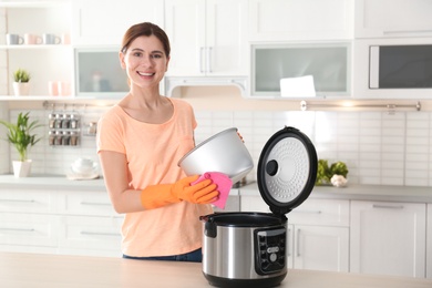 Woman cleaning modern multi cooker at table in kitchen