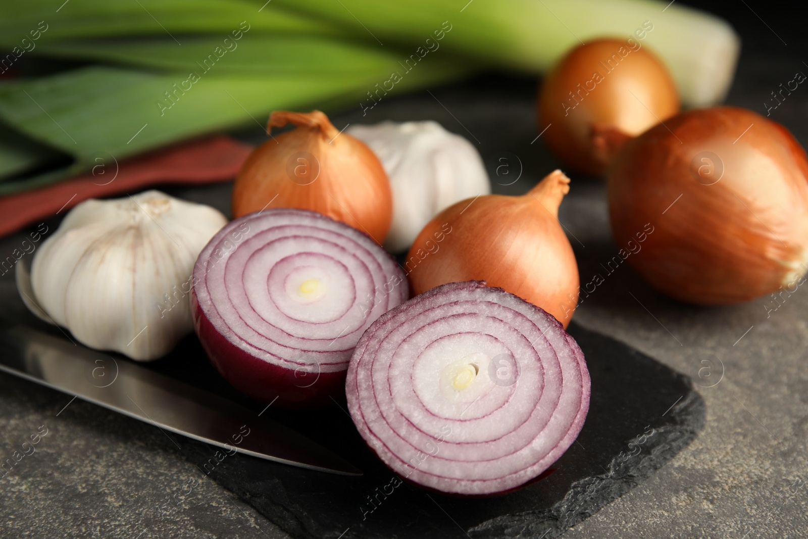 Photo of Fresh whole and cut onions, leeks, garlic on grey table, closeup