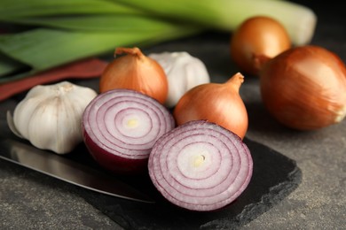 Fresh whole and cut onions, leeks, garlic on grey table, closeup