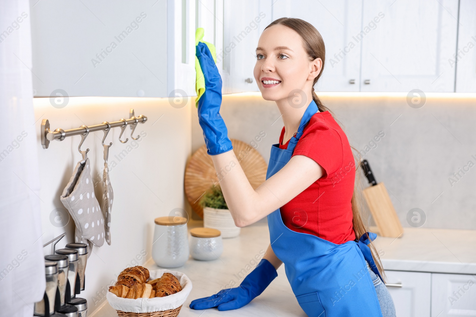 Photo of Woman cleaning cabinet with rag in kitchen