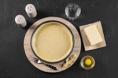 Photo of Pie tin with fresh dough and ingredients on black table, flat lay. Making quiche