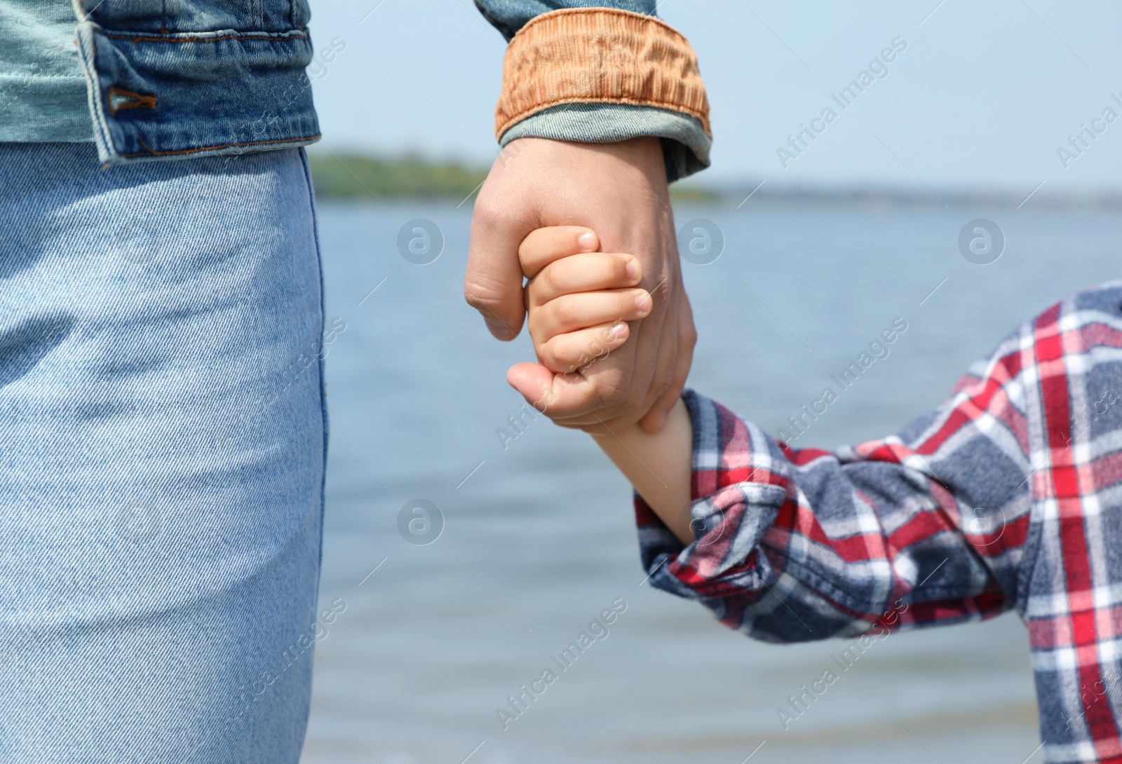 Photo of Little child holding hands with his father near river, closeup