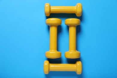 Photo of Yellow dumbbells on light blue background, flat lay. Morning exercise