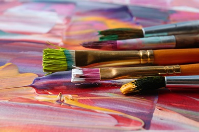 Photo of Set of different brushes on abstract colorful paint, closeup