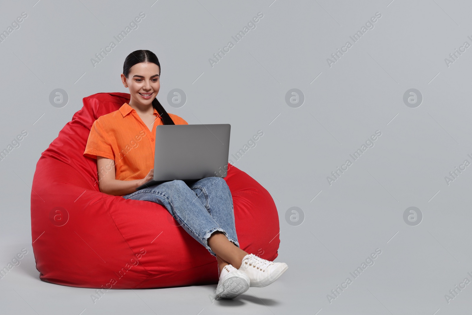 Photo of Happy woman with laptop sitting on beanbag chair against light gray background