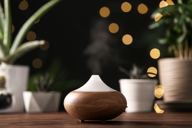 Photo of Composition with modern essential oil diffuser on wooden table against blurred lights, space for text