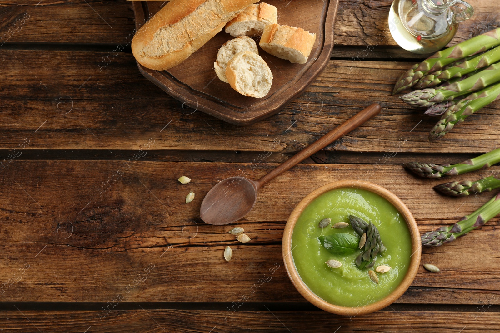 Photo of Delicious asparagus soup in bowl served on wooden table, flat lay