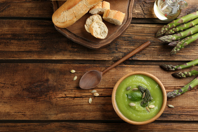 Delicious asparagus soup in bowl served on wooden table, flat lay