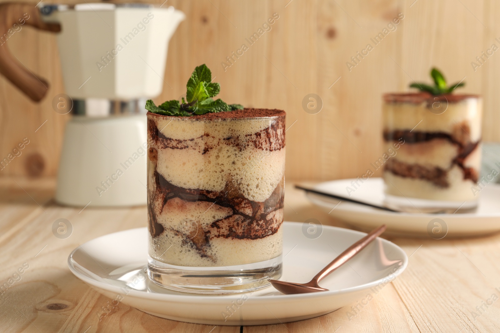 Photo of Tasty tiramisu and mint in glasses on light wooden table, closeup