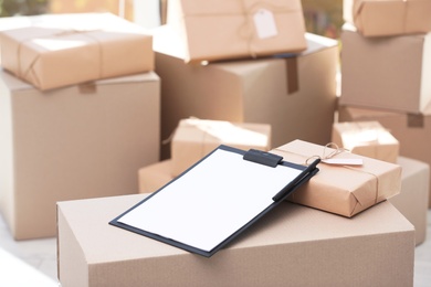 Clipboard, parcel with tag and blurred stacked boxes on background, indoors