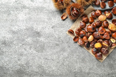 Photo of Delicious roasted edible chestnuts on grey table, flat lay. Space for text