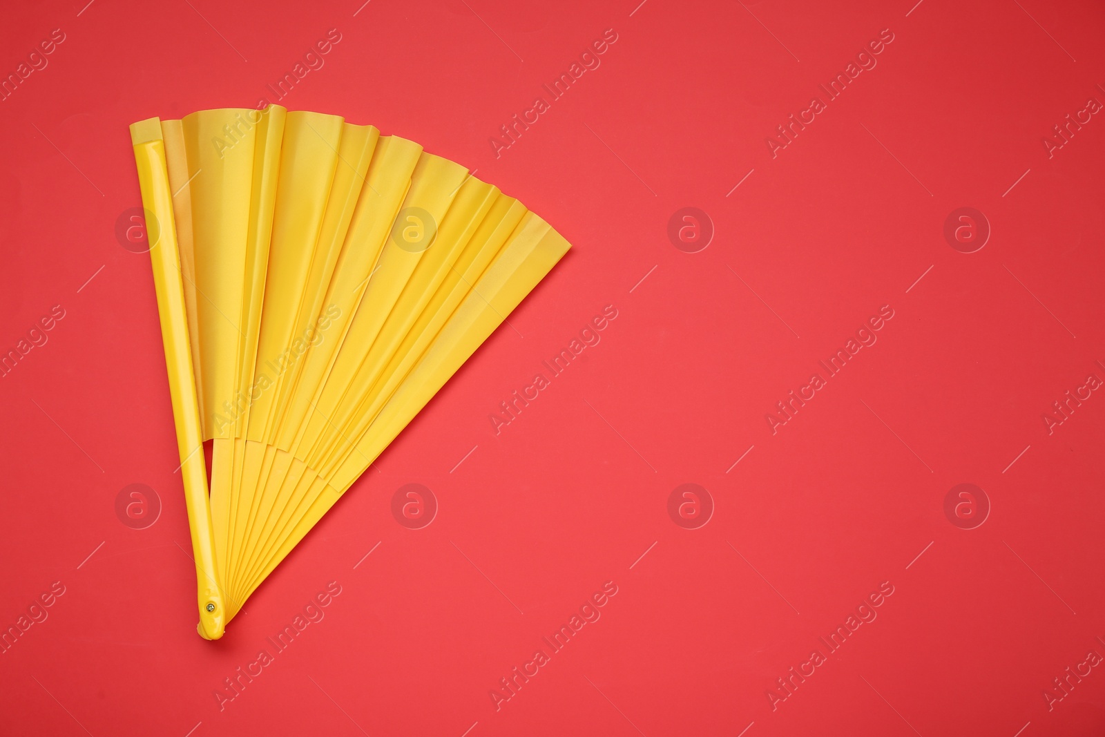 Photo of Bright yellow hand fan on red background, top view. Space for text