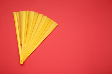 Bright yellow hand fan on red background, top view. Space for text