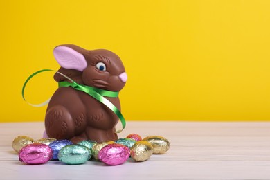 Chocolate Easter bunny and eggs on white wooden table against yellow background. Space for text