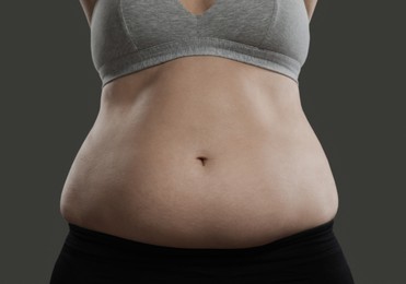 Woman with excessive belly fat on grey background, closeup. Overweight problem