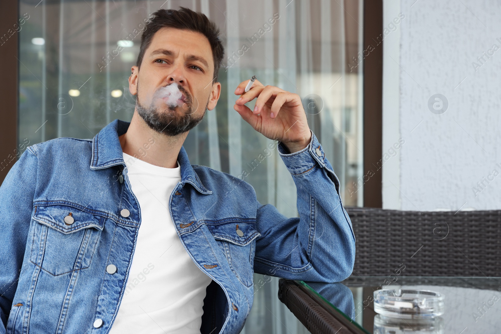 Photo of Handsome man smoking cigarette at table in outdoor cafe