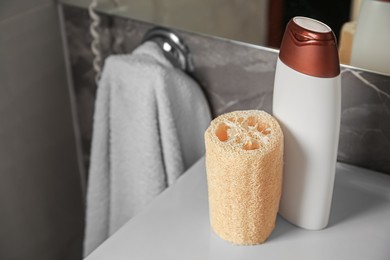 Natural loofah sponge and bottle with shower gel on washbasin in bathroom. Space for text