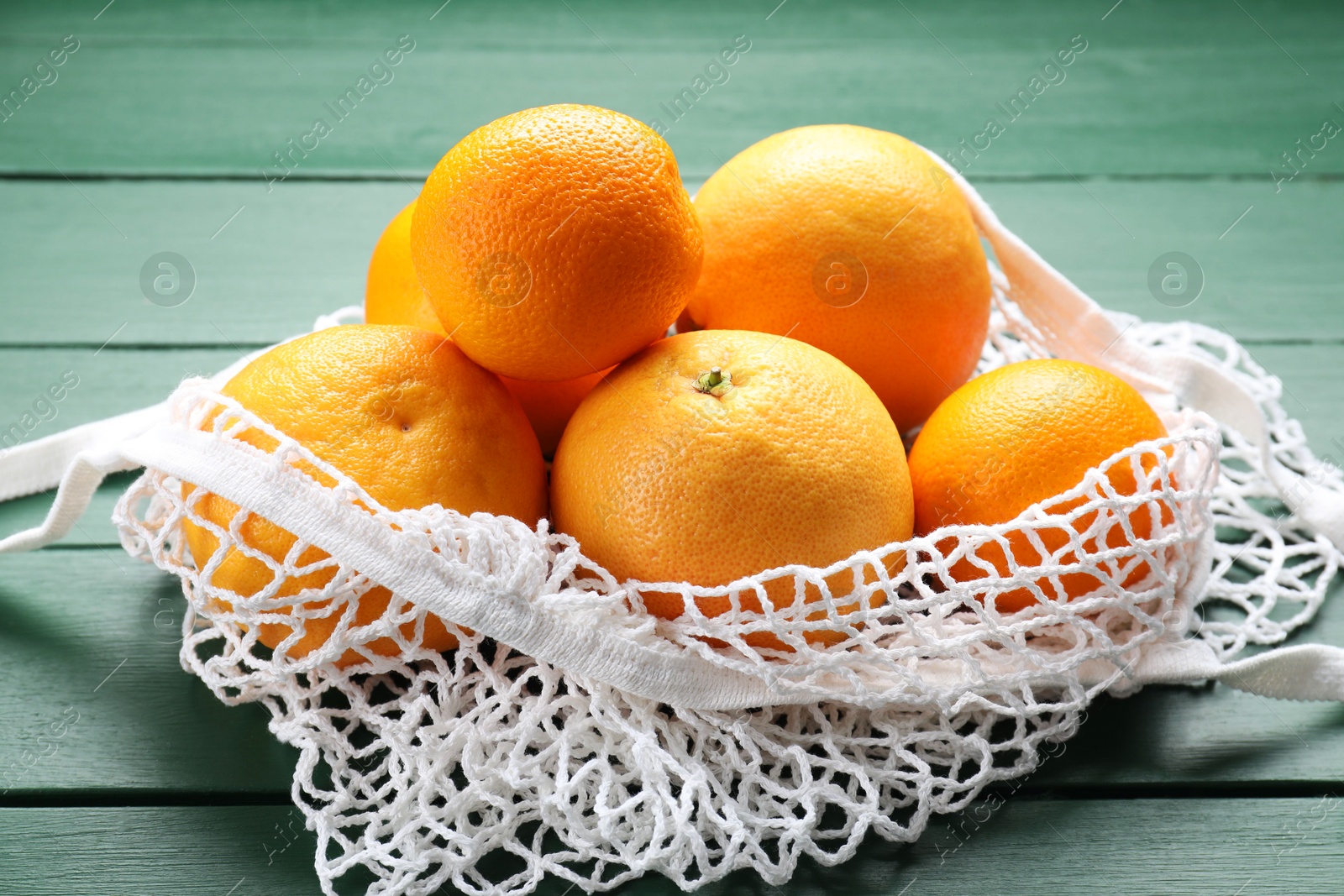 Photo of String bag with oranges on green wooden table, closeup