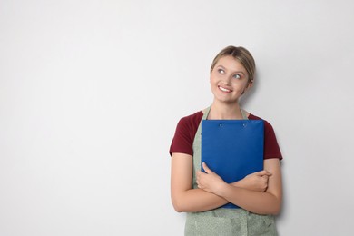 Photo of Beautiful young woman in clean apron with clipboard on light grey background. Space for text