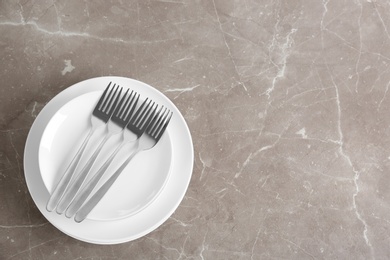 Stack of ceramic dishware with cutlery on grey background, top view