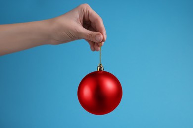 Woman holding red Christmas ball on light blue background, closeup. Space for text