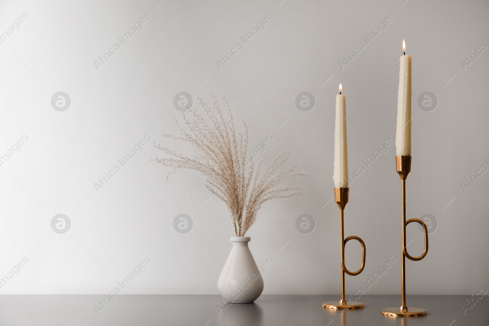 Photo of Burning candles and vase on grey table near white wall, space for text