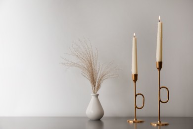 Burning candles and vase on grey table near white wall, space for text