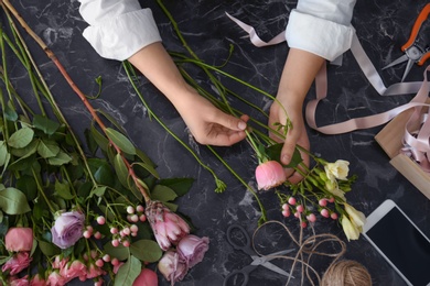 Female florist creating beautiful bouquet at table, top view