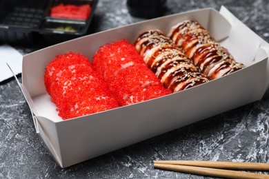 Paper box with delicious sushi rolls on grey textured table. Food delivery