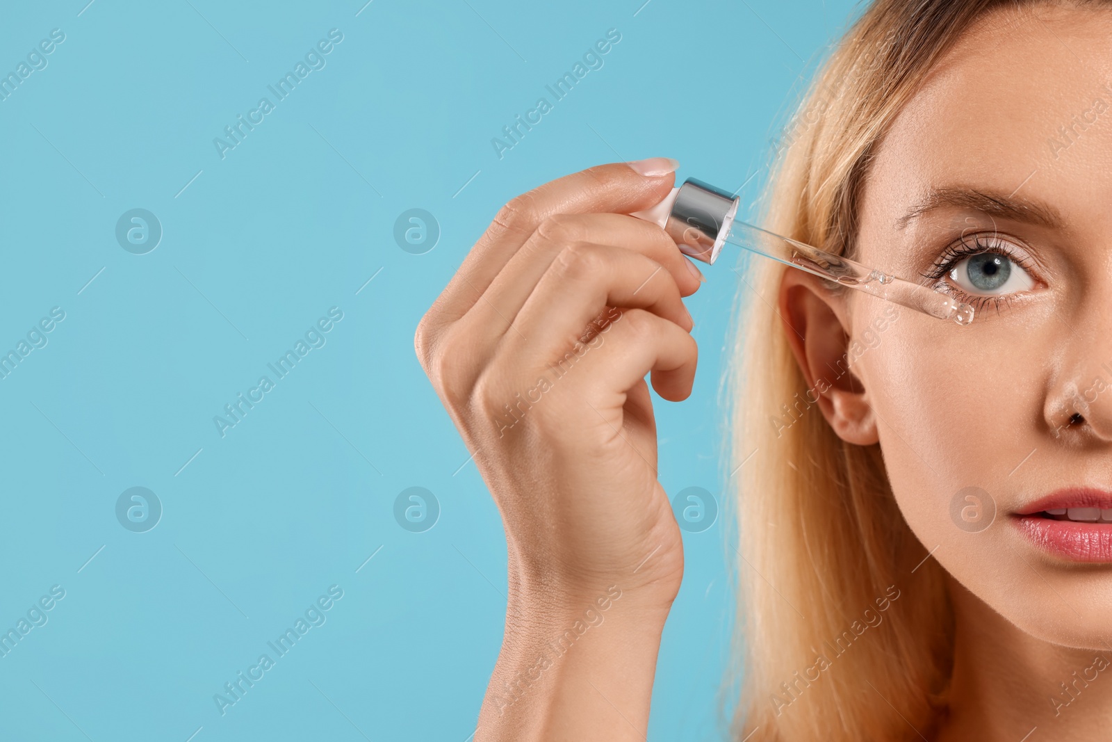 Photo of Beautiful woman applying cosmetic serum onto her face on light blue background, closeup. Space for text