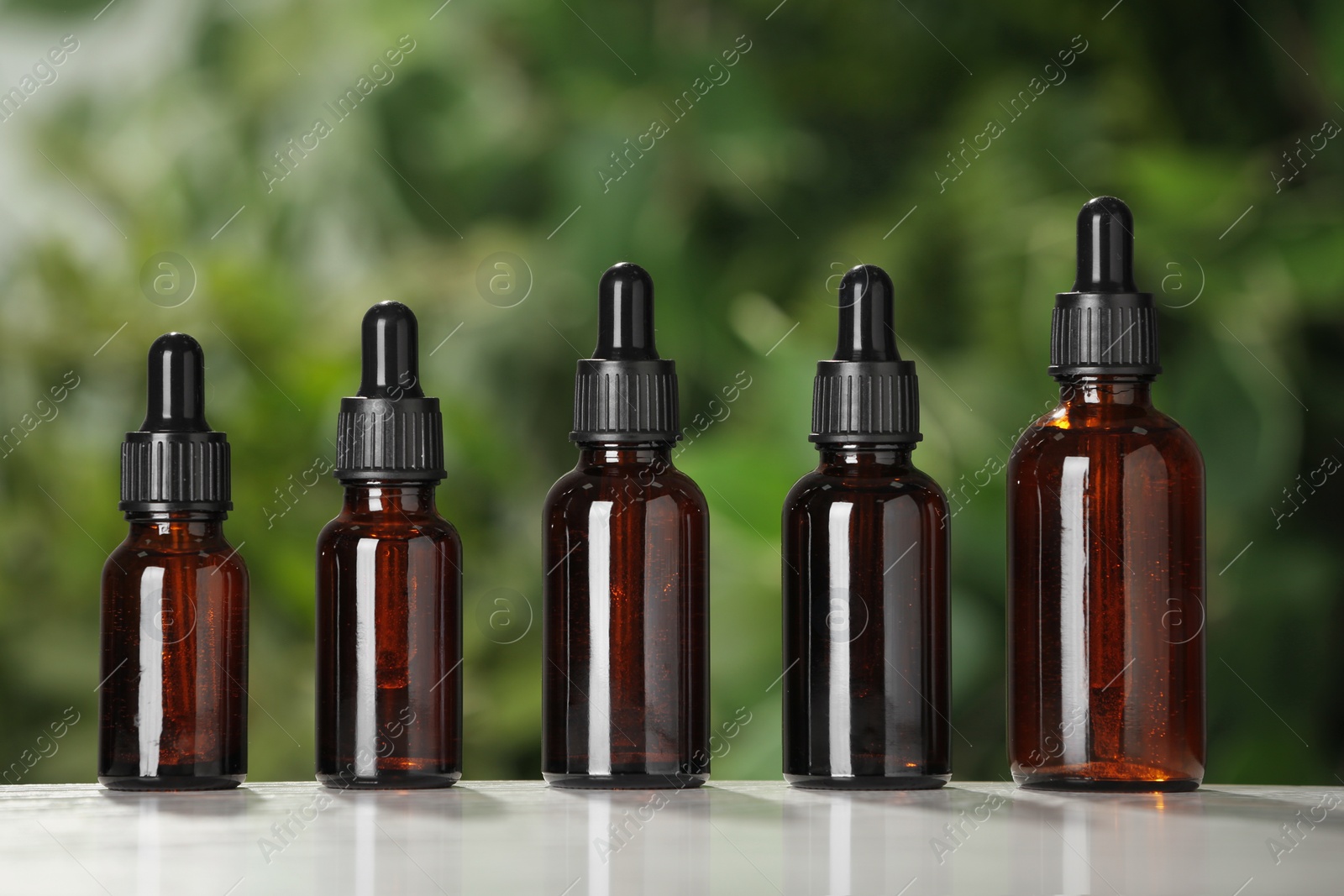 Photo of Glass bottles on white table against blurred green background