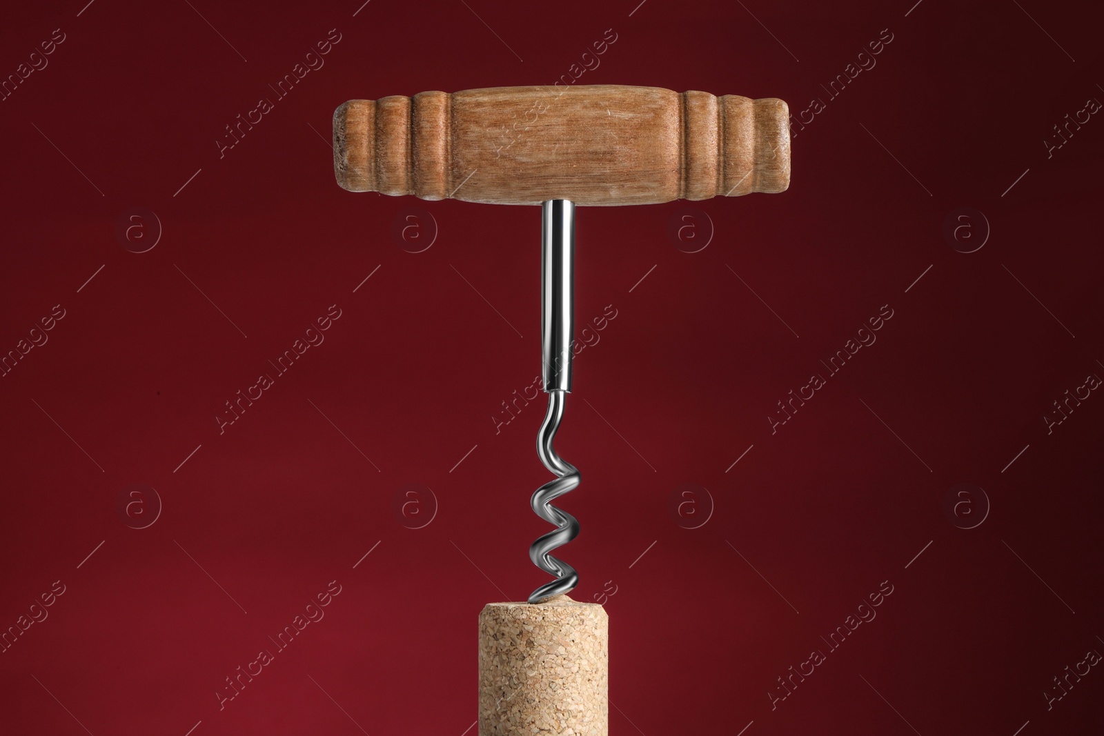 Photo of Corkscrew with cork against dark red background, closeup