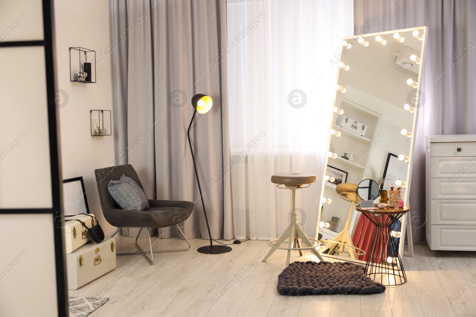 Photo of Makeup room. Stylish mirror with light bulbs, beauty products on table and chair indoors