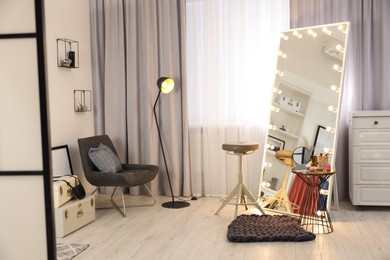 Makeup room. Stylish mirror with light bulbs, beauty products on table and chair indoors