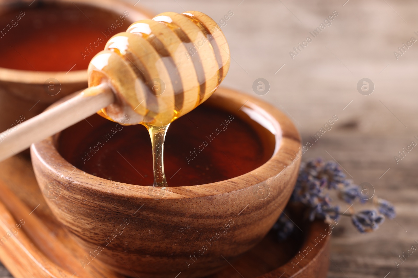 Photo of Pouring delicious honey from dipper into bowl on wooden table, closeup