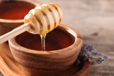 Pouring delicious honey from dipper into bowl on wooden table, closeup