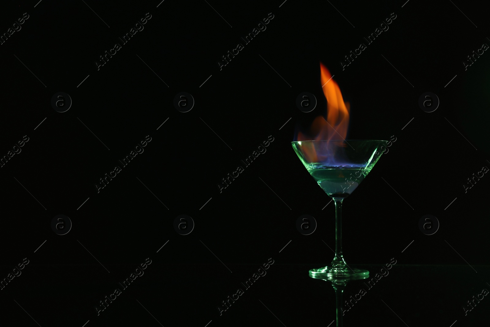 Photo of Cocktail glass with flaming vodka on black background, space for text