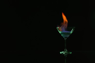 Photo of Cocktail glass with flaming vodka on black background, space for text