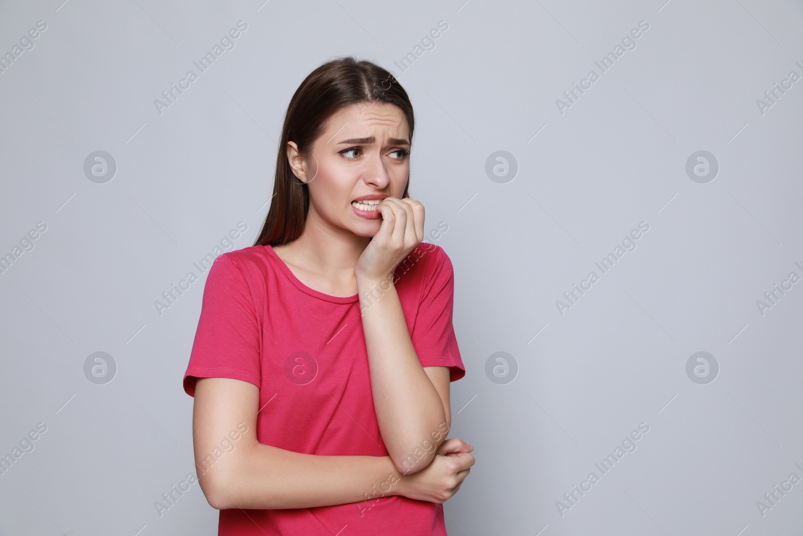 Photo of Young woman biting her nails on light grey background. Space for text