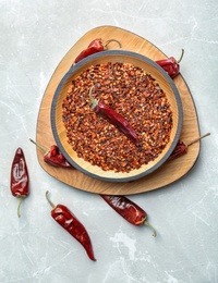 Photo of Bowl with crushed chili pepper and pods on light background