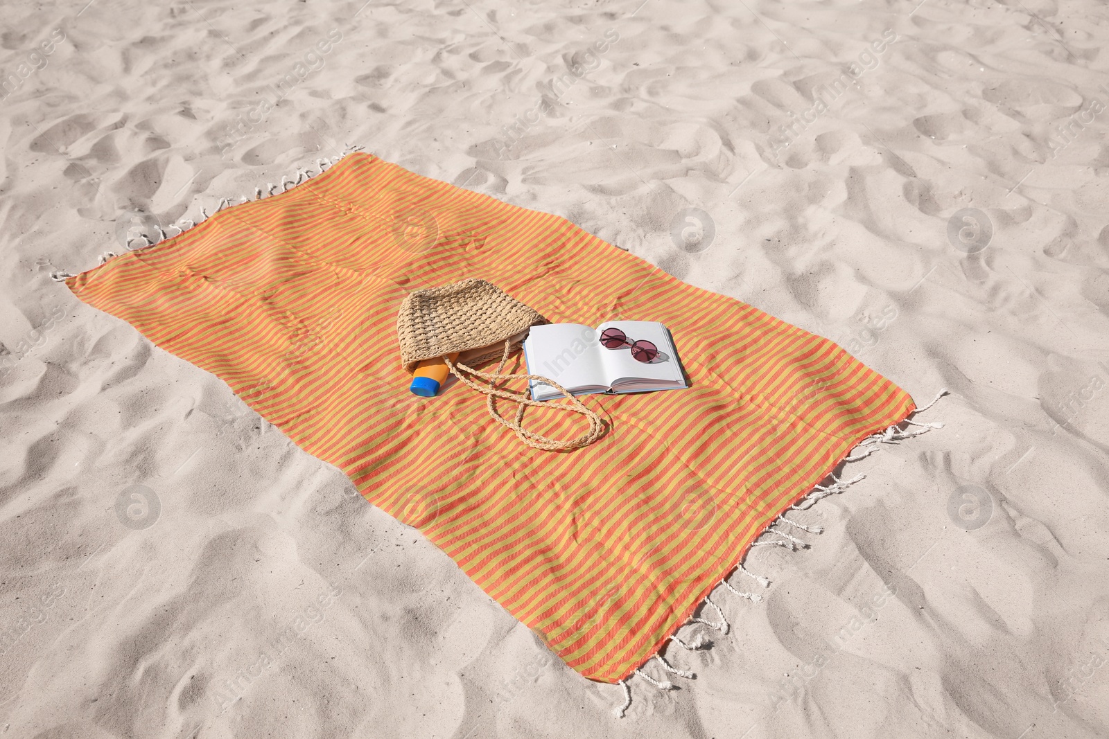 Photo of Orange striped beach towel with bag, accessories and book on sand