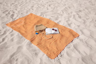 Orange striped beach towel with bag, accessories and book on sand