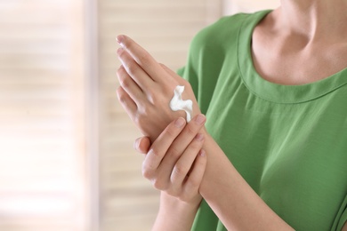 Photo of Young woman applying cream on her hands indoors, closeup