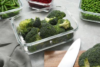 Photo of Containers with broccoli and fresh products on light gray table, closeup. Food storage