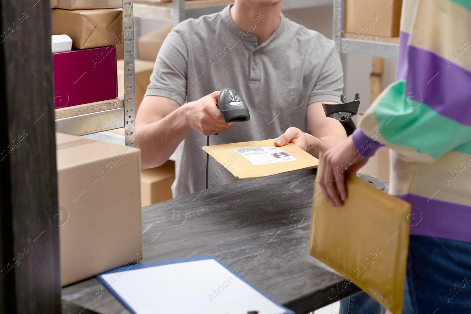 Photo of Woman and post office worker with scanner reading parcel barcode at counter indoors, closeup