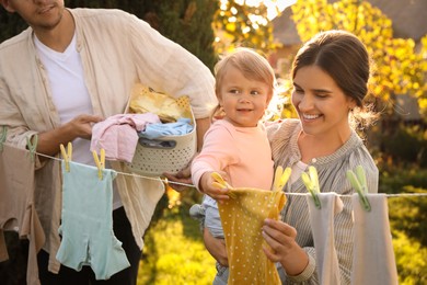 Photo of Happy family hanging baby clothes with clothespins on washing line for drying in backyard