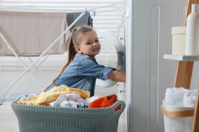 Little girl putting dirty clothes into washing machine in bathroom