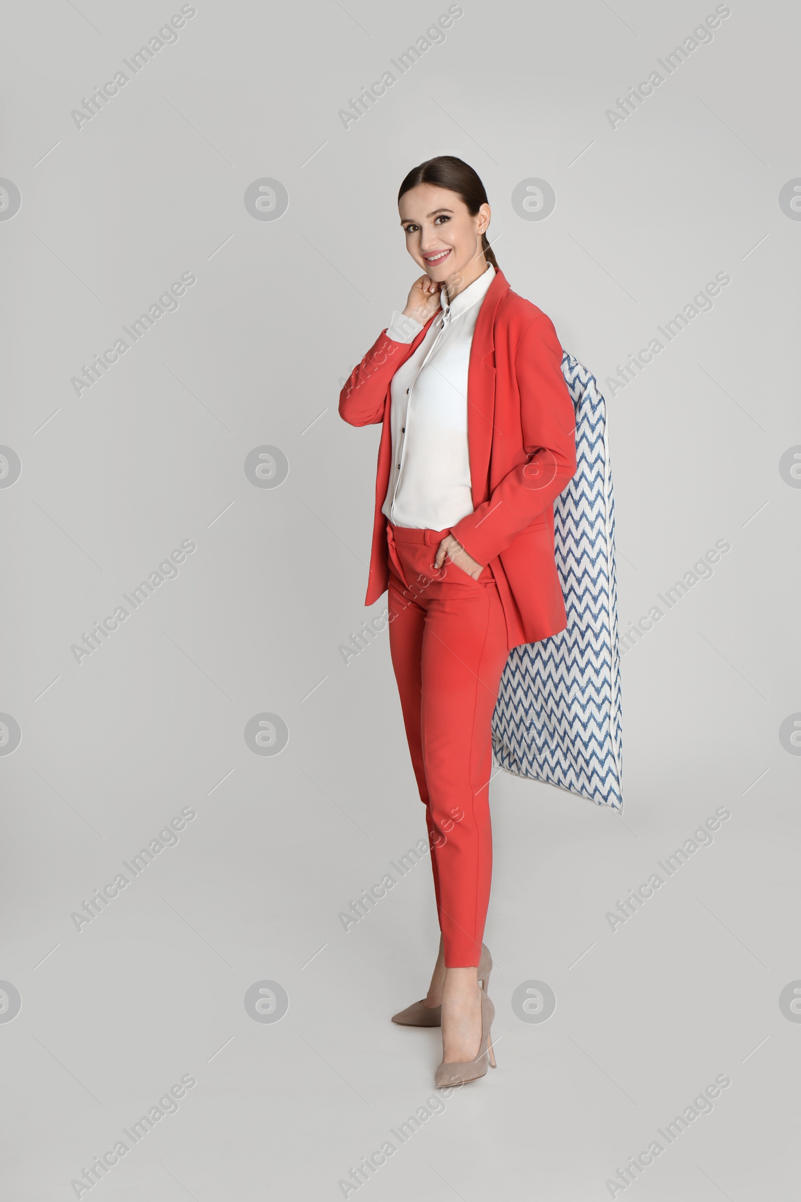 Photo of Young woman holding hanger with clothes in garment cover on light grey background. Dry-cleaning service